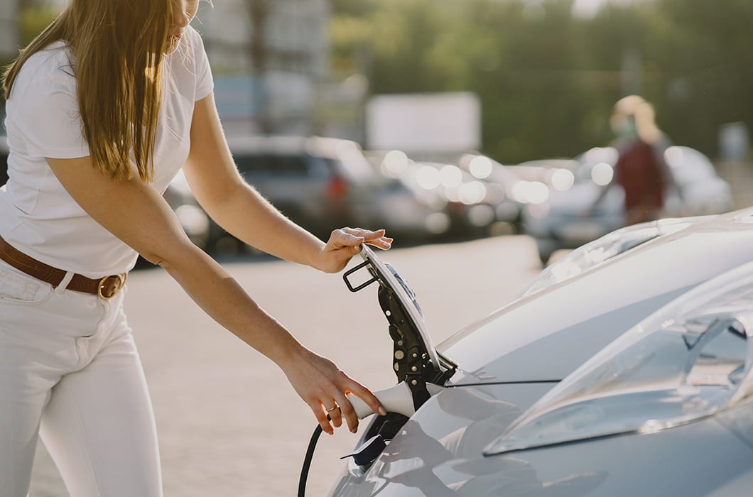 Woman Charging Ev In Parking Lot 1060x700px